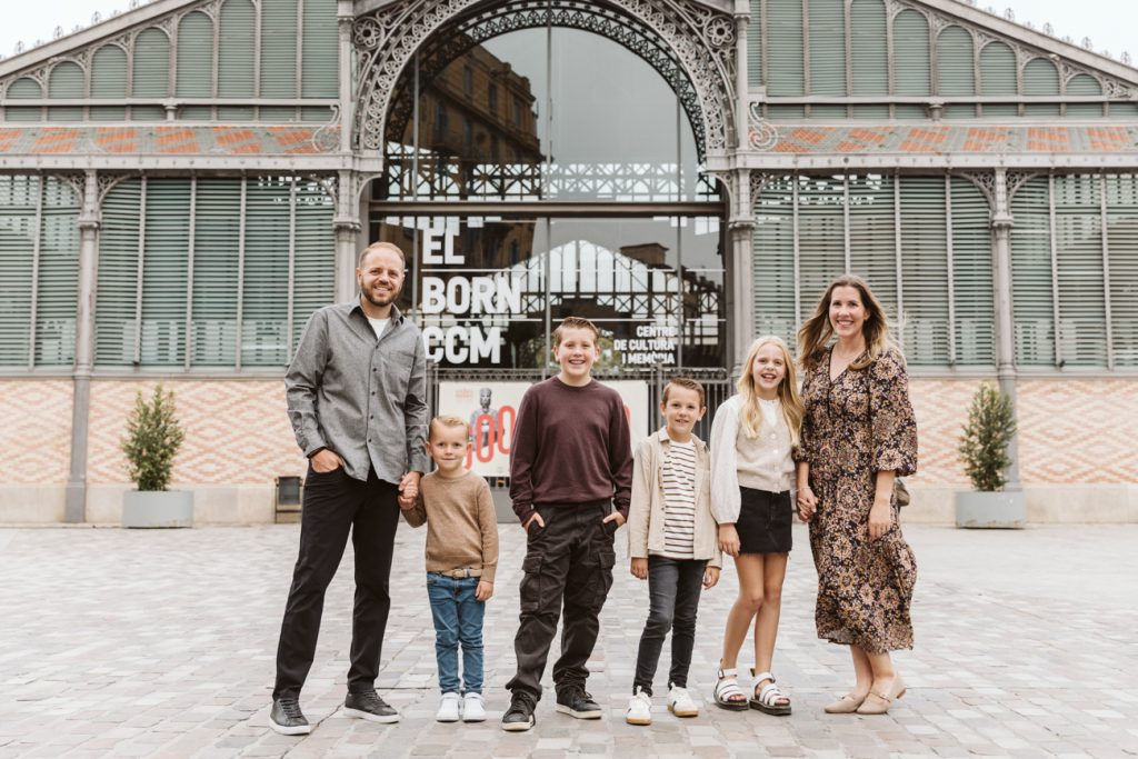 A family of six—two adults and four children—stands smiling in front of the El Born Centre de Cultura i Memòria, one of the 5 iconic locations for family photoshoot in Barcelona. They pose together on a cobblestone plaza in coordinated outfits.