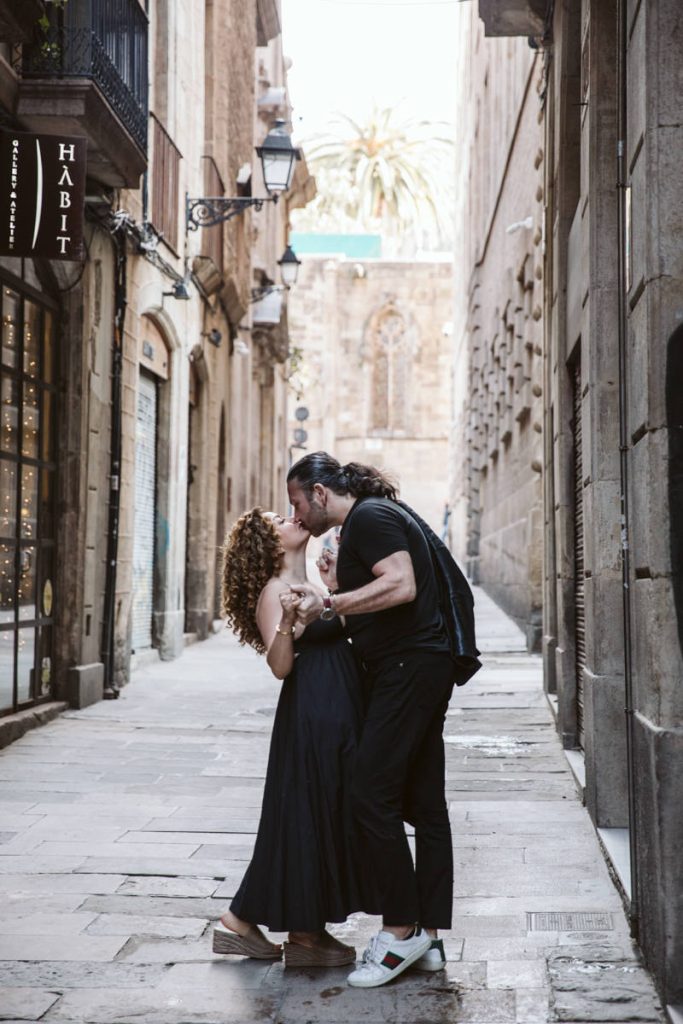 A couple dances closely and smiles at each other on a narrow, cobblestone street lined with historic buildings and ornate lamps—perfect for family photos in the Gothic Quarter in Barcelona, capturing a romantic atmosphere.