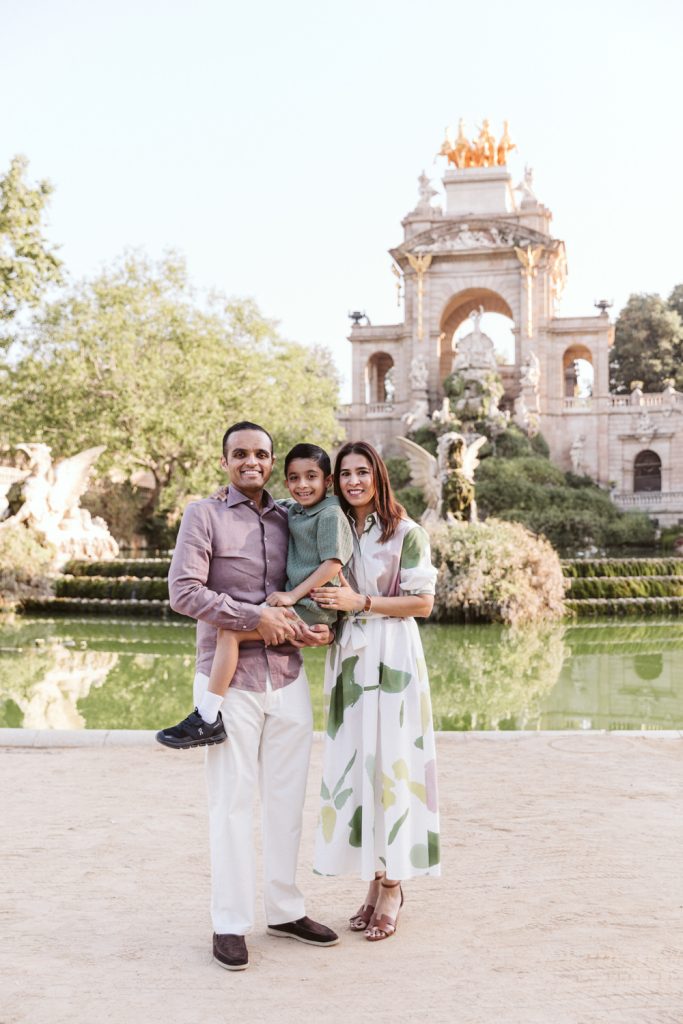 Family in soft neutral outfits posing during a photo session in fronto fo the fountain in Ciutadella Park, surrounded by greenery.