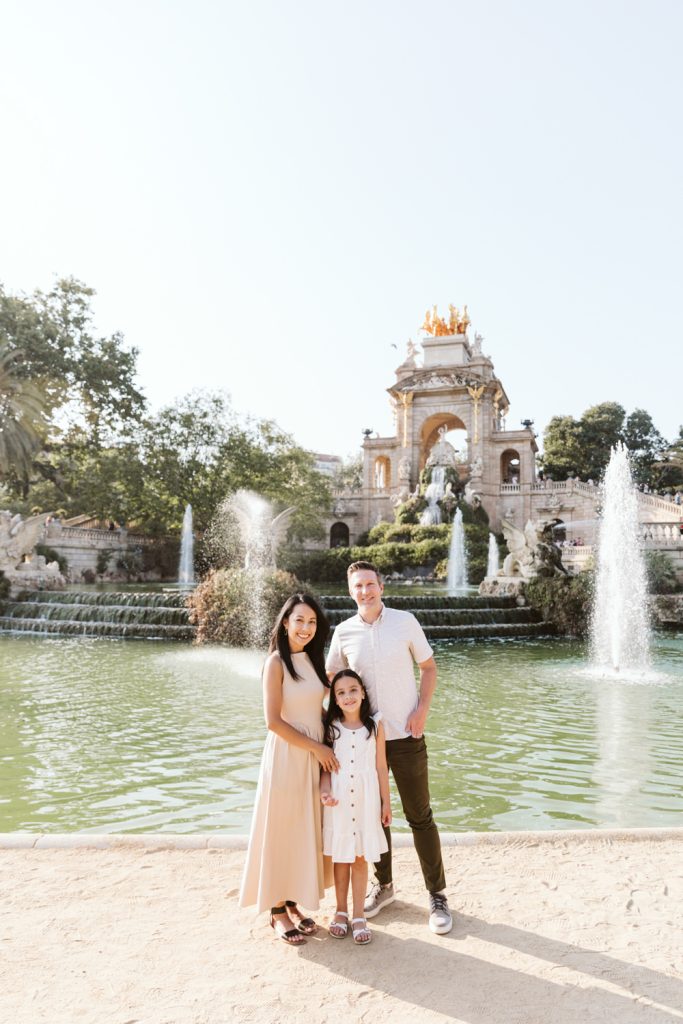 Family in soft neutral outfits during a photo session in Ciutadella Park, surrounded by greenery.