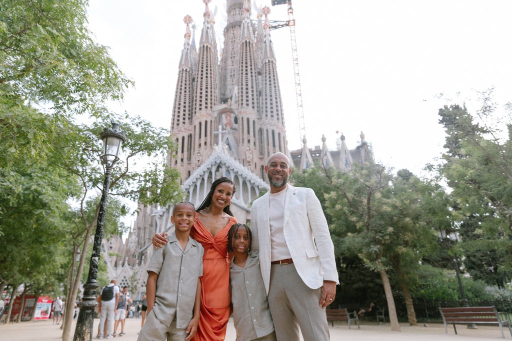 A family posing for photos in front of Sagrada Familia in Barcelona, wearing beige soft tones, with the mother wearing orange dress that pops.